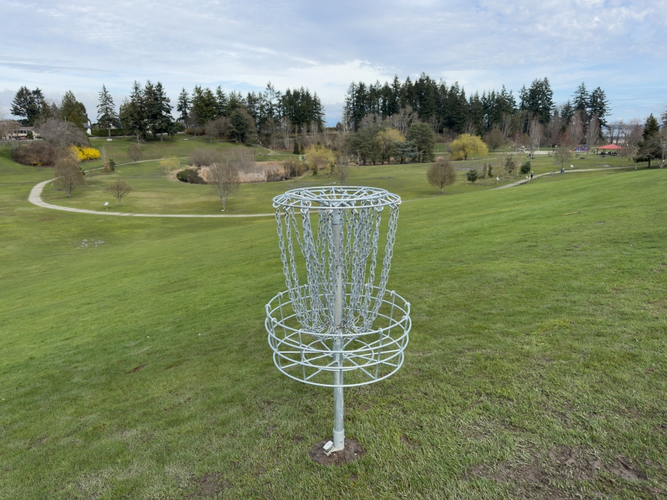 A new disc golf hole sits atop a hill at Diefenbaker Park, overlooking the grassy field.